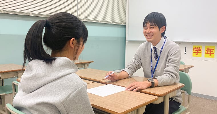 教室で講師が笑顔で生徒に個別に説明している様子。