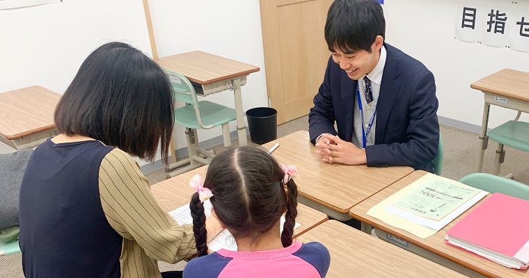 講師が机越しに生徒と保護者に面談している様子。